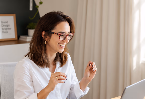A woman smiling at her laptop at a light wooden desk