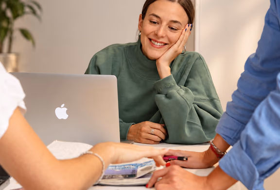 A woman resting her chin on her hand, smiling across a table